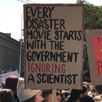 Person carrying placard which reads every disaster movie starts with the government ignoring the scientist