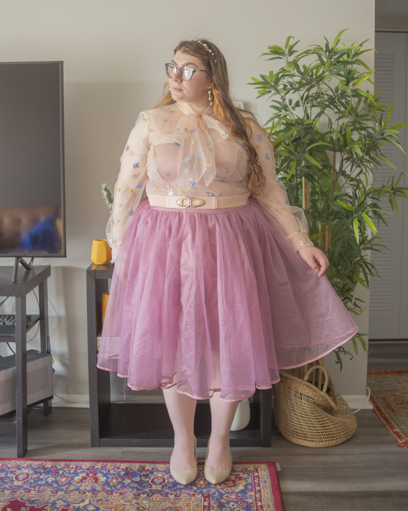 An outfit consisting of a white sheer bow blouse with pastel sequin flowers, with a pastel pink metallic tube top under, tucked into a pink tulle skirt and cream slingback heels.