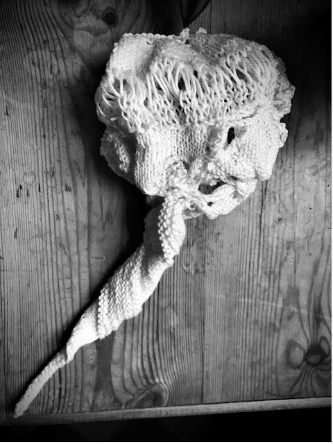 cream knitted piece, bunched abstract knitting formed in the shape of a cerebrum, cerebellum and brainstem displayed diagonally top left to bottom right on a knotted wooden surface.