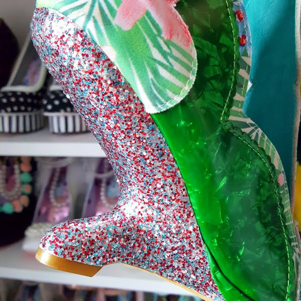 close up of heel-less glitter wedge heel on shoe with shoe shelves in background