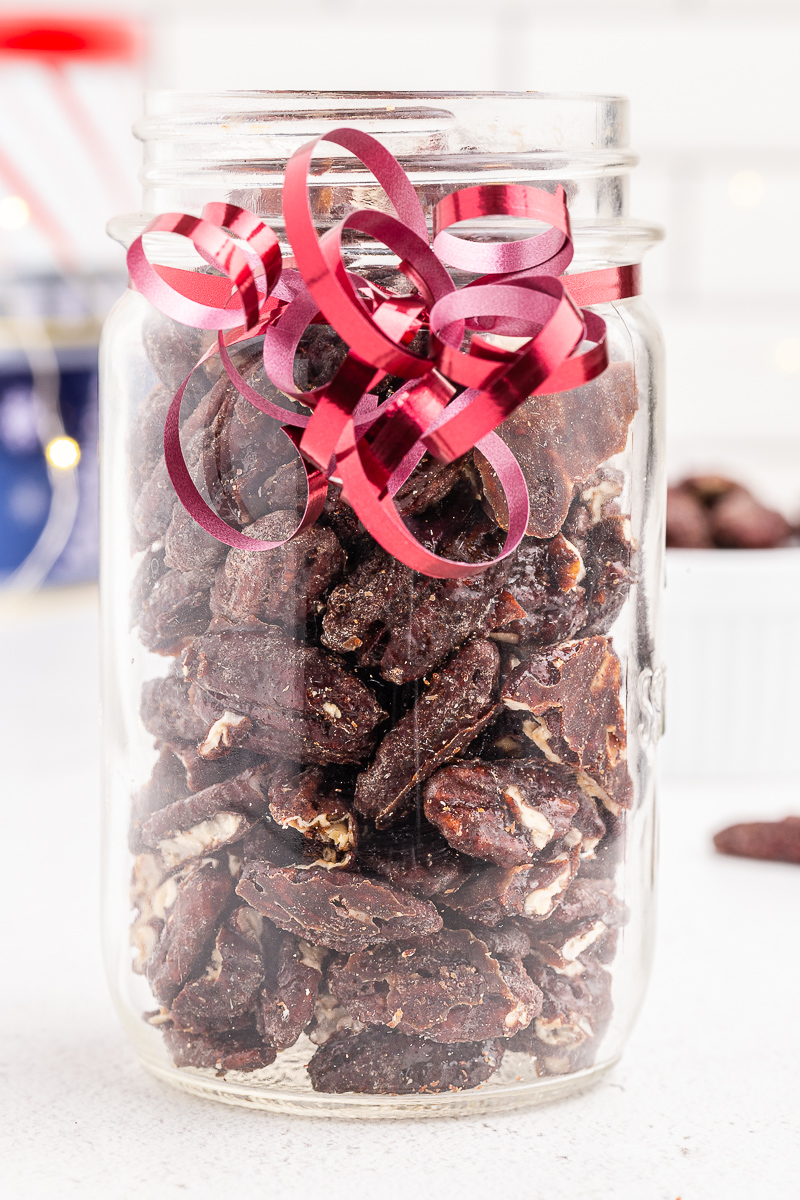 Photo of Keto Candied Pecans in a glass jar with red ribbon around it.