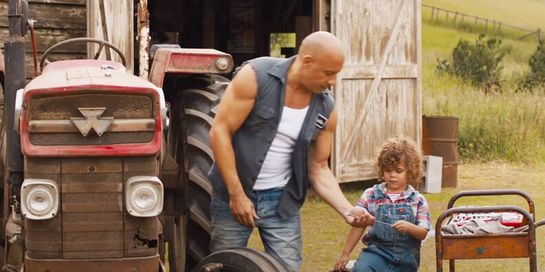 Na imagem vemos 2 personagens, sendo pai e filho e um lugar no campo, ao lado deles há um trator vermelho e de fundo uma casa de madeira e em um ambiente aberto