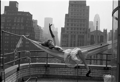 black and white photograph of dancer Gwen Verdon lounging in a hammock on a balcony overlooking the New York skyline in 1953