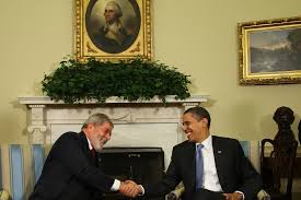 o ex-presidente Lula dando um aperto de mão no ex-presidente dos Estados Unidos Barack Obama, os dois estão sentados e de terno.