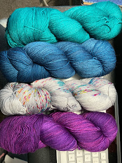 four hanks of yarn, top to bottom: bright teal, cerulean blue, light grey multi-color speckles, and a deep, vibrant violet
