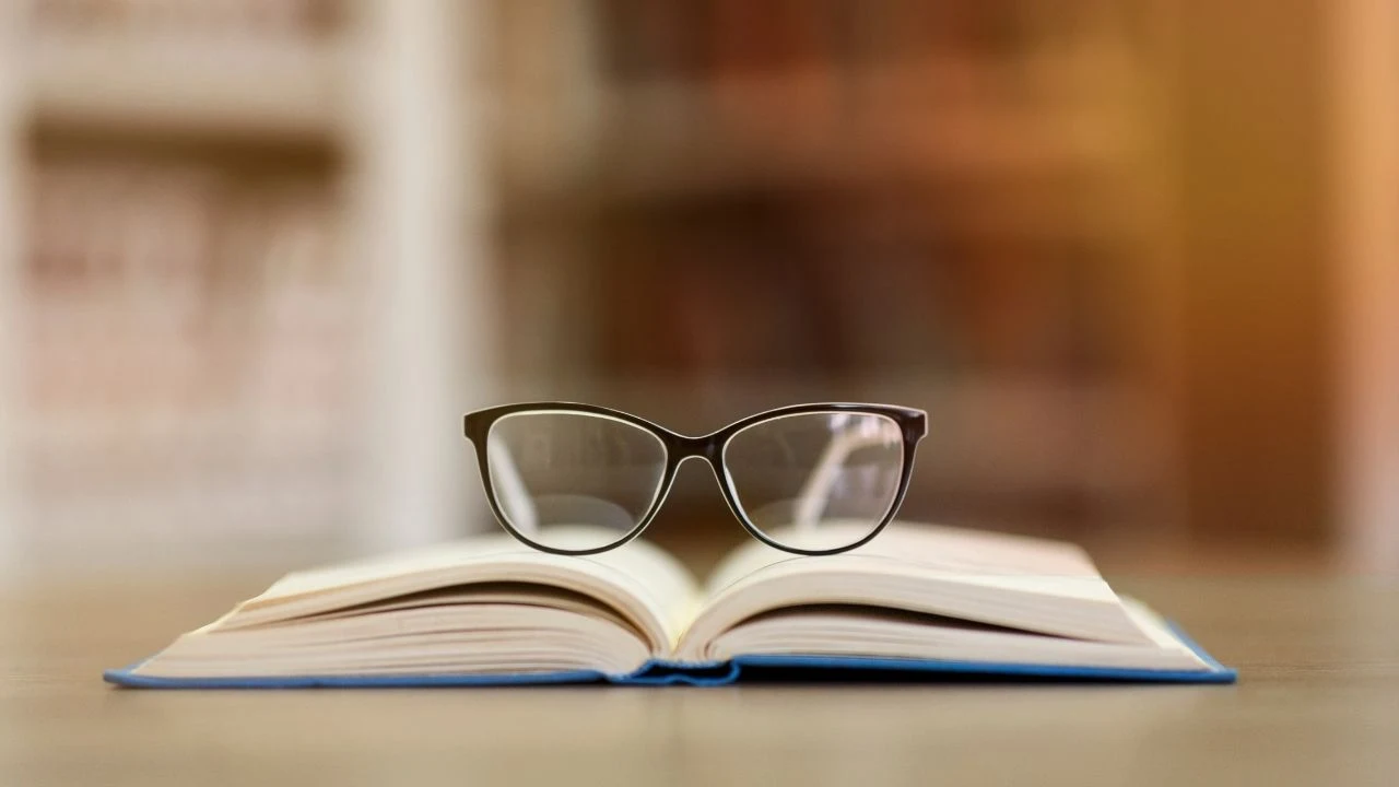 Concept of education. Soft focus of stylish glasses lying on open book in library, blurred bookshelves.
