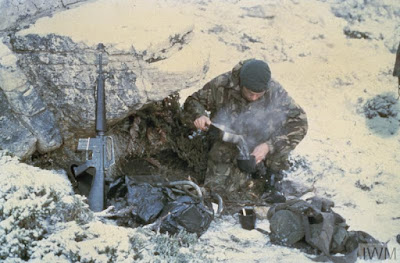 A Royal Marine Commando brewing up in the mountains around Port Stanley his weapon a 5.56mm Armalite indicates that he may well be a member of the Mountain and Arctic Warfare Cadre