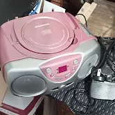 Pink radio with black speakers next to a black cahrging cable.