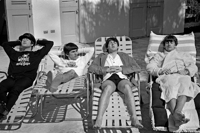 black and white photograph of The Beatles lounging on pool chairs at swimming pool in Miami, 1964