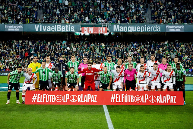 REAL BETIS BALOMPIÉ y RAYO VALLECANO DE MADRID. Temporada 2021-22. Claudio Bravo, Mario Suárez, Antonio Sánchez Sánchez (cuarto árbitro), Edgar, Juan Martínez Munuera (árbitro), Pathé Ciss, Willian José, Óscar Trejo, Germán Pezzella, Sergi Guardiola, Catena, Miguel Martínez Munuera (linier), Guido Rodríguez. Fekir, Isi, Juanmi, Sabaly, Álex Moreno, Luca Zidane, Sergio Canales, Fran García, Pau Cebrián Devis (linier), Álvaro García, Óscar Valentín, Balliu y William Carvalho. Los dos conjunto y el equipo arbitral posan con el lema #FútbolporlaPaz promovido por la RFEF con motivo de la invasión militar de Rusia en Ucrania.REAL BETIS BALOMPIÉ 1 RAYO VALLECANO DE MADRID 1 Global eliminatoria: REAL BETIS 3 RAYO VALLECANO 2 Jueves 03/03/2022, 21:00 horas. Copa del Rey, semifinales, partido de vuelta. Sevilla, estadio Benito Villamarín: 50.916 espectadores. GOLES: 0-1: 80’, Bebé. 1-1: 90*2’, Borja Iglesias. ENTRENADORES: Real Betis: Manuel Pellegrini. Rayo Vallecano: Andoni Iraola. ÁRBITRO: Juan Martínez Munuera, Comité Valenciano.