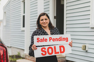 Real Estate Agent Standing in Black Printed Blouse Holding a Sale Pending Signage