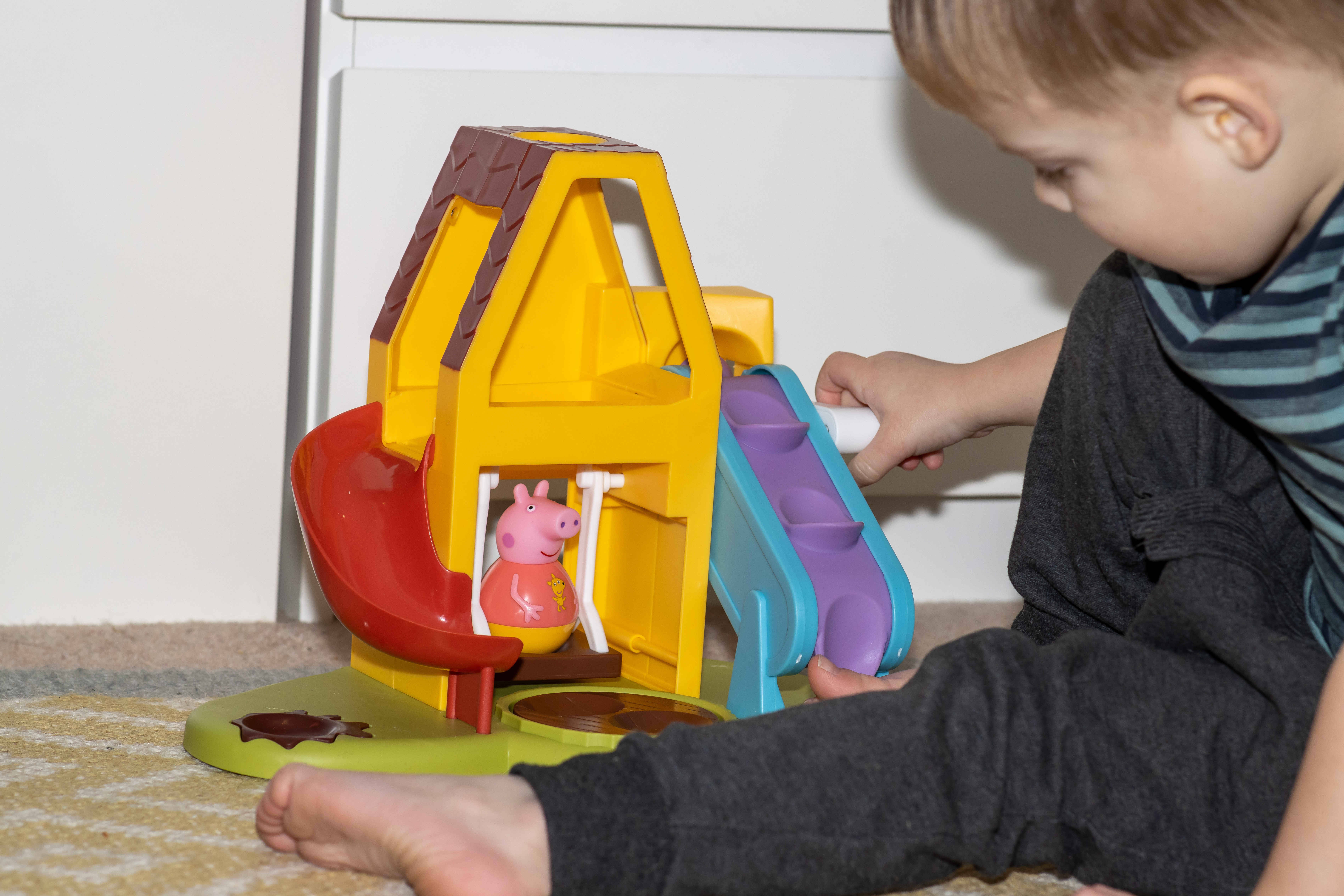 A toddler playing with the Peppa Pig Weebles wobble and wind playhouse. He is winding the lever so Peppa rocks on the swing