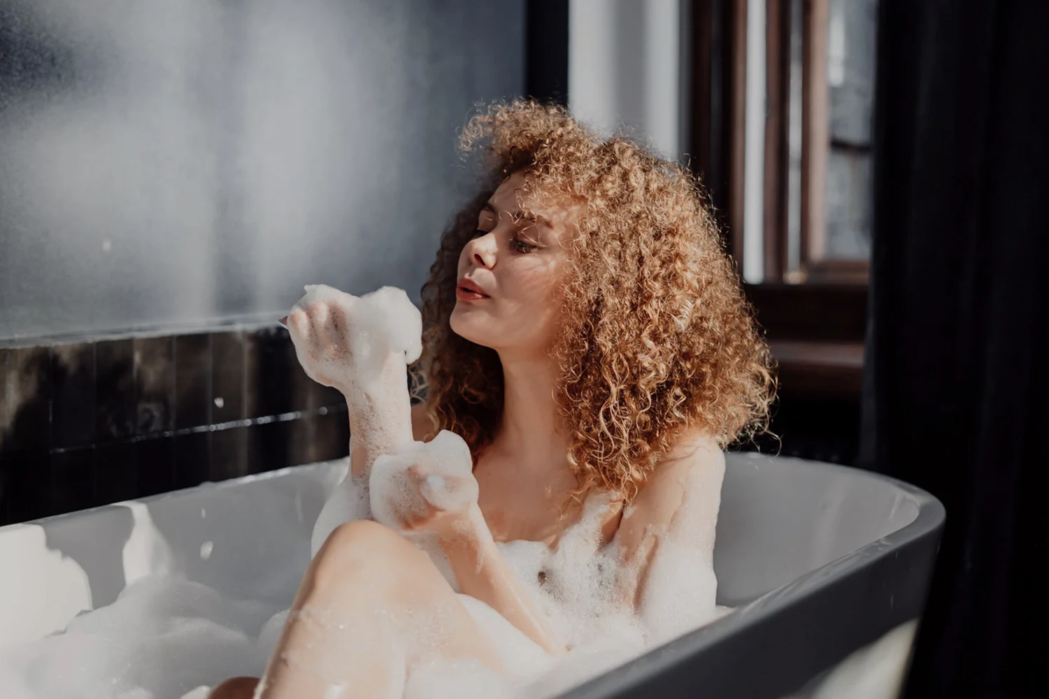 curly woman takes bubble bath and poses for the camera