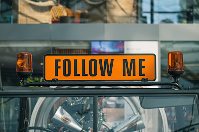 A sign that has the words Follow me on top of car