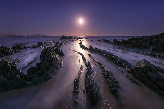 ocaso lunar sobre los flysch de la playa de barrika con las rocas emergiendo del agua