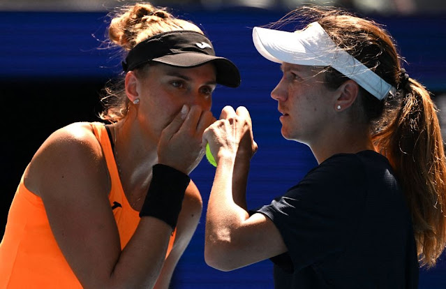 Bia Haddad Maia, de laranja e Anna Danilina, de azul escuro, conversando ao pé do ouvido na final do Australian Open