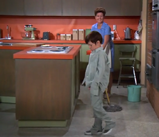 Bobby Brady walks sadly in the kitchen while Alice cheerfully mops.