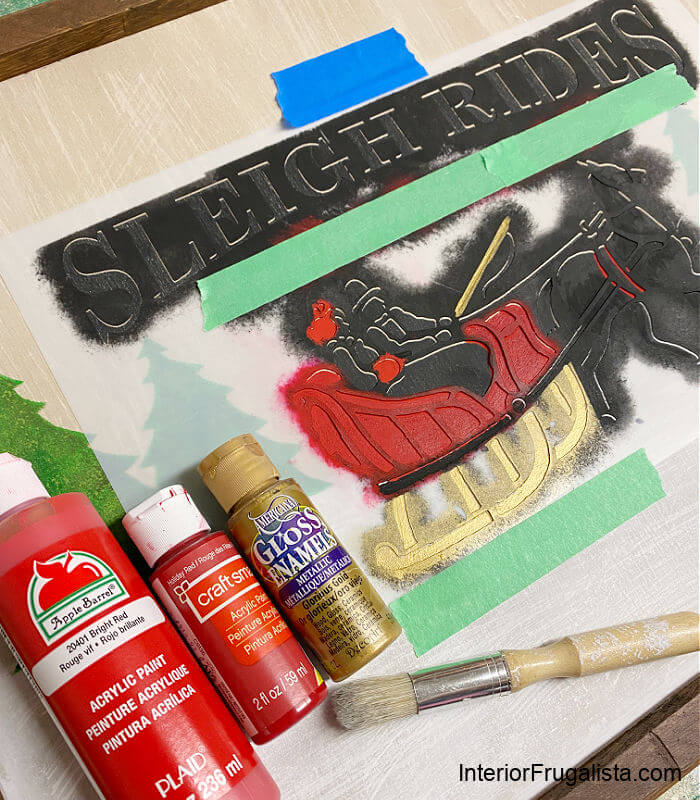 Stenciling the horse drawn sleigh ride sign with red, green, and metallic gold craft paint.