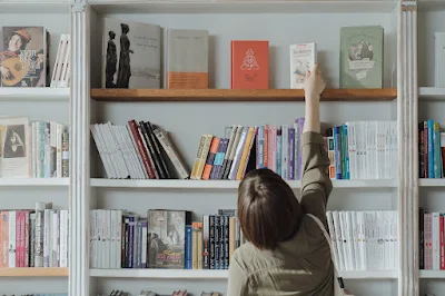 seorang perempuan mengambil buku di rak
