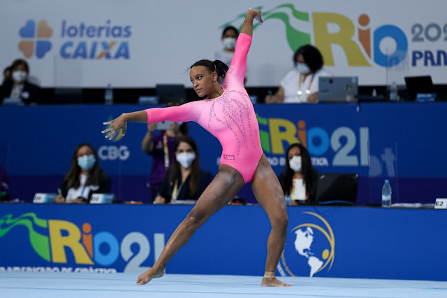Rebeca Andrade abre os braços durante coreografia. Ela veste um collant rosa. Ao fundo, um painel escrino Panamericano Rio 2021
