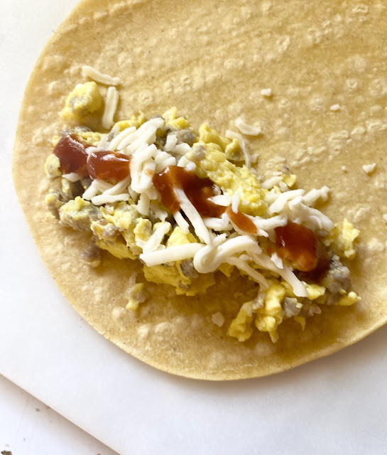 Close up view of corn tortilla topped with eggs, sausage and cheese.