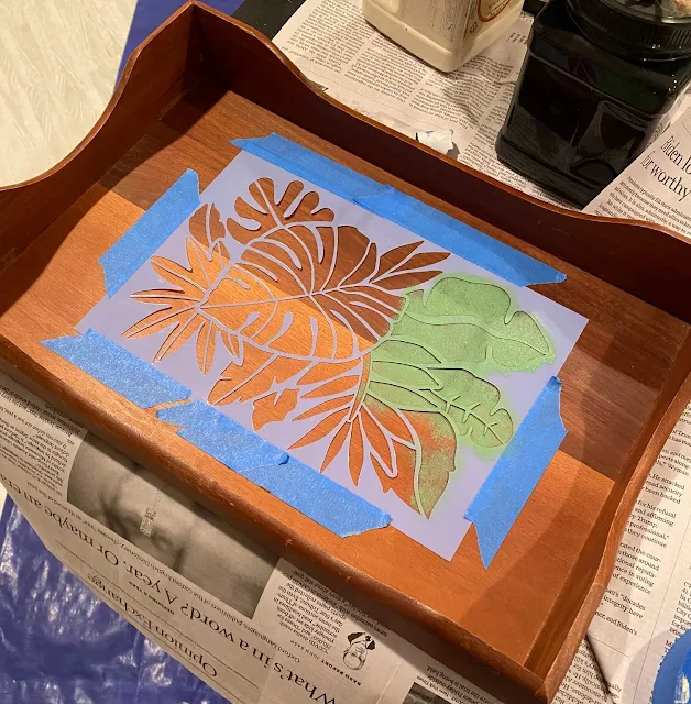 Photo of a tropical leaf stencil being stenciled on a wooden tray.