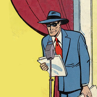 A man in a blue suit and fedora with red tie and domino mask leans over a 1940s style radio microphone. He holds a few loose papers. The background is yellow and a burgundy curtain hangs behind him.