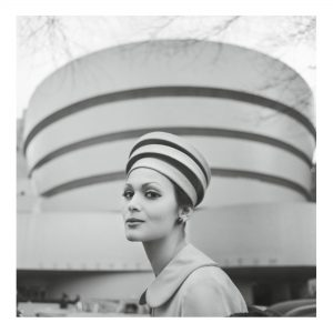 model wearing an architectural hat resembling the Guggenheim Museum in front of the Guggenheil Museum