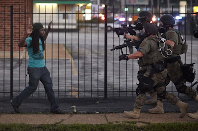 A ma backs away as St. Louis County police officers approach him with guns drawn and eventually arrest him in Ferguson, Missouri, on Aug. 11, 2014;