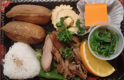 Bento lunch with inari sushi, onigiri, chicken, orange slice, egg roll, Jello, seaweed salad