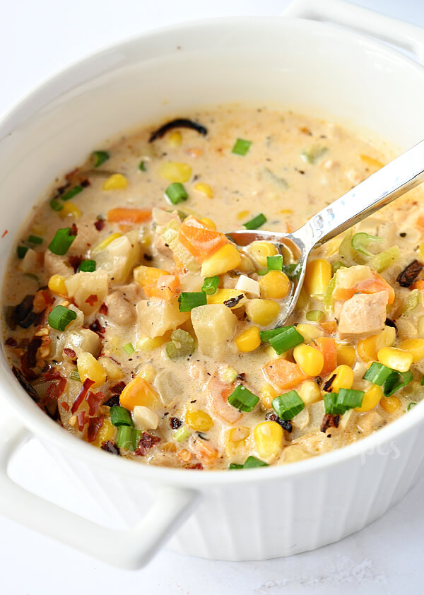 a white dutch oven with  chicken corn chowder with scallions, chicken, corn, carrots and celery