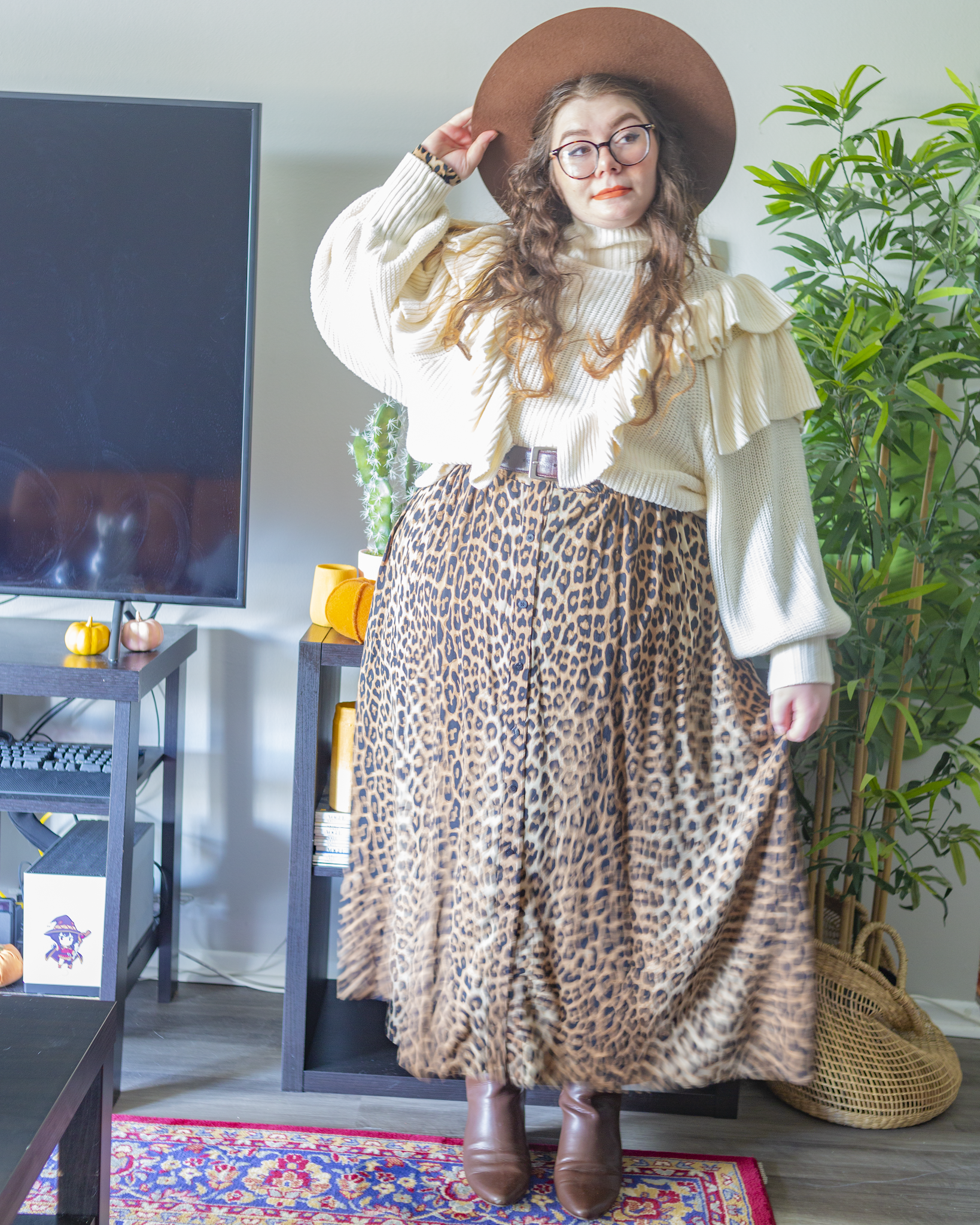 An outfit consisting of a white long dolman sleeve sweater with ruffles on the chest, over a long sleeve brown animal print shirt maxi dress with brown midi boots.