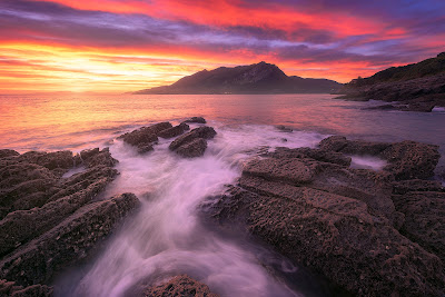 rojo amanecer sobre una cala de piedra en sonabia