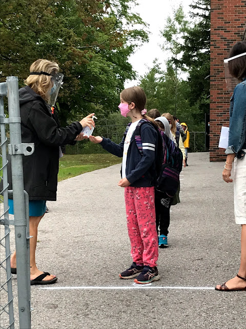 First day of school with kids lined up to get hand sanitizer from a teacher