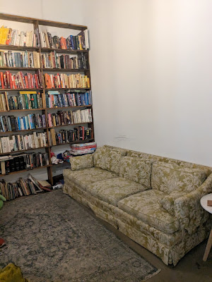 a comfy couch sits in front of a tall bookshelf arranged in rainbow order at Art SUX