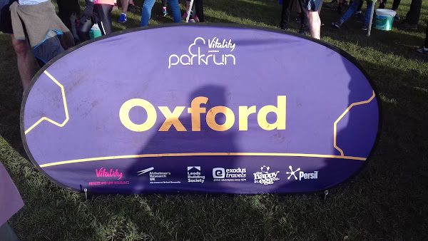 A popup sign for Oxford parkrun with a crowd in the background