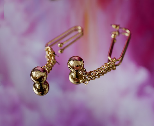 A pair of gold dangling earrings set against a glossy purple background