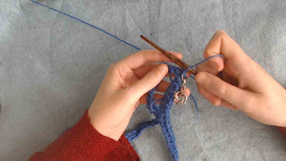 someone holding a few rounds of single crochet in the round.  They're working with a wooden crochet hook, and a stitch marker with a dolphin charm is clipped into the work.