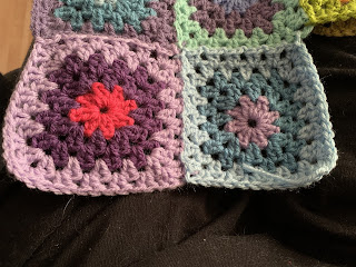 Two multicoloured granny squares attached to a previous row of squares. The photo is focused on the two new squares so we only see the edges of the previous ones.