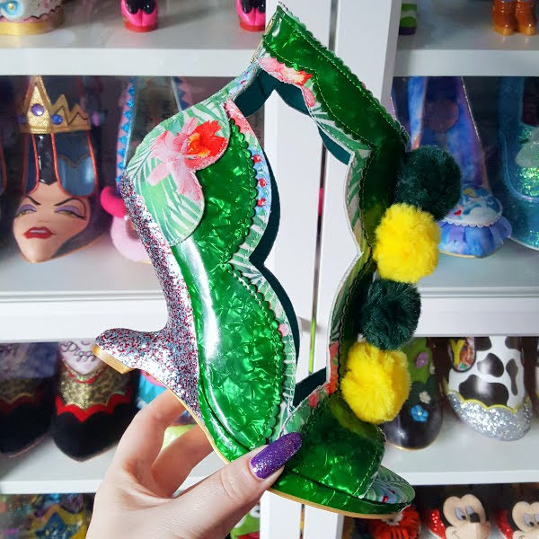 Irregular Choice green Carni Val shoe held in hand in front of shoe shelves