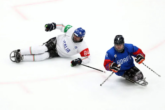 Jogador da Itália, usando unifome branco, e jogador da Coreia, de azul, em cima de seus trenós