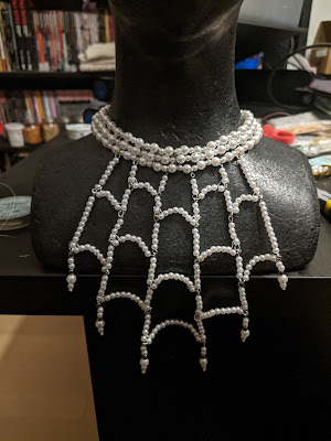 Photo of strings of pearl beads arranged into a necklace that looks like a spiderweb attached to a pearl choker