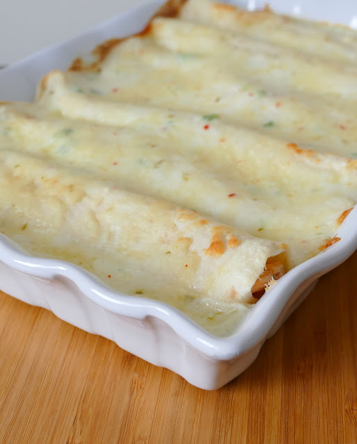 Enchiladas in a white casserole with melted cheese on top.