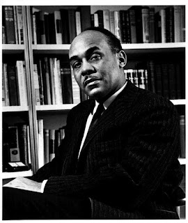 Black and white portrait of Ralph Waldo Ellison against a bookshelf lined with books.