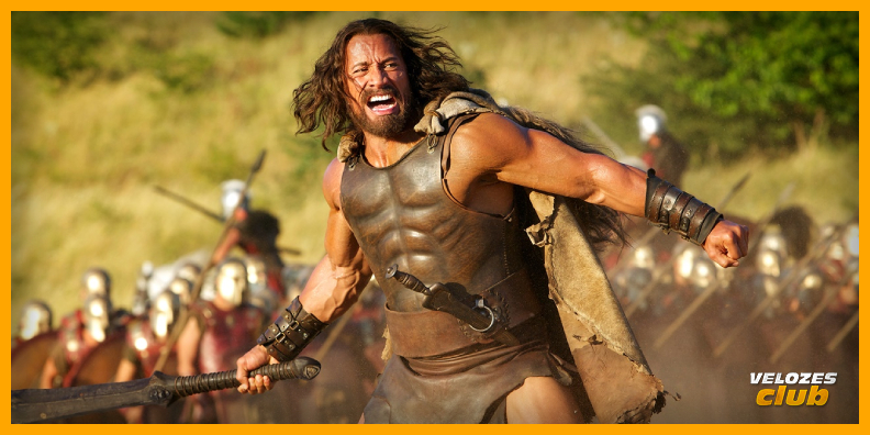 The Rock no personagem Hércules, lutando com uma espada contra guerreiros. Ele tem em seu rosto uma expressão de raiva