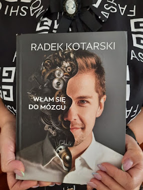 Czytelniczka w czarnej sukience w białe napisy z kameą prezentuje książkę Radka Kotarskiego pod tytułem Włam się do mózgu.