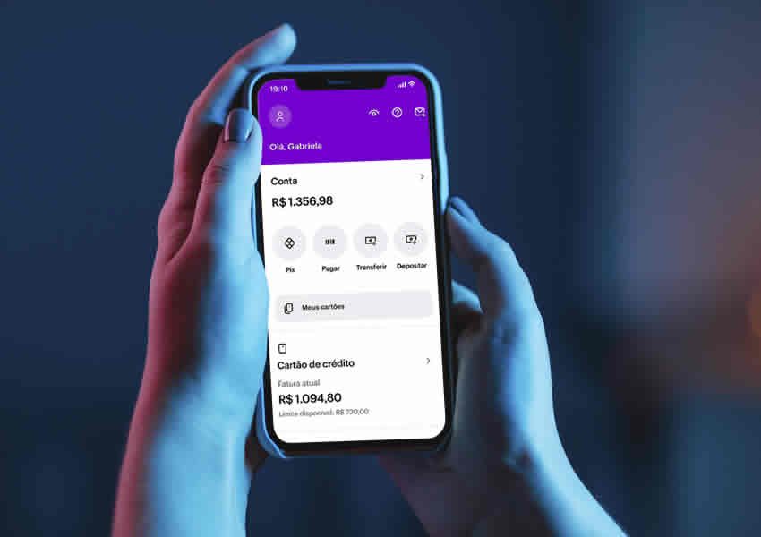 Imagem mostra duas mãos segurando um smartphone onde mostra o app do banco digital nubank aberto.