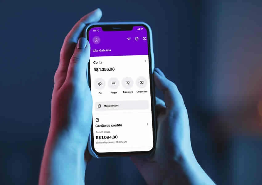 Imagem mostra duas mãos segurando um smartphone onde mostra o app do banco digital nubank aberto.