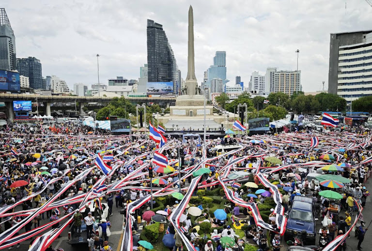 Bangkok protesters rally amid Thai flags, ribbons, and umbrellas, demanding ouster.