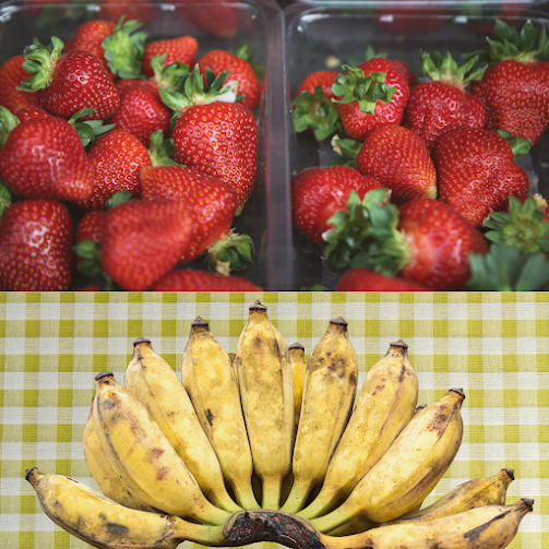 Buah strawberi ranum di dalam bekas plastik dan pisang terlebih masak diatas meja alas kuning